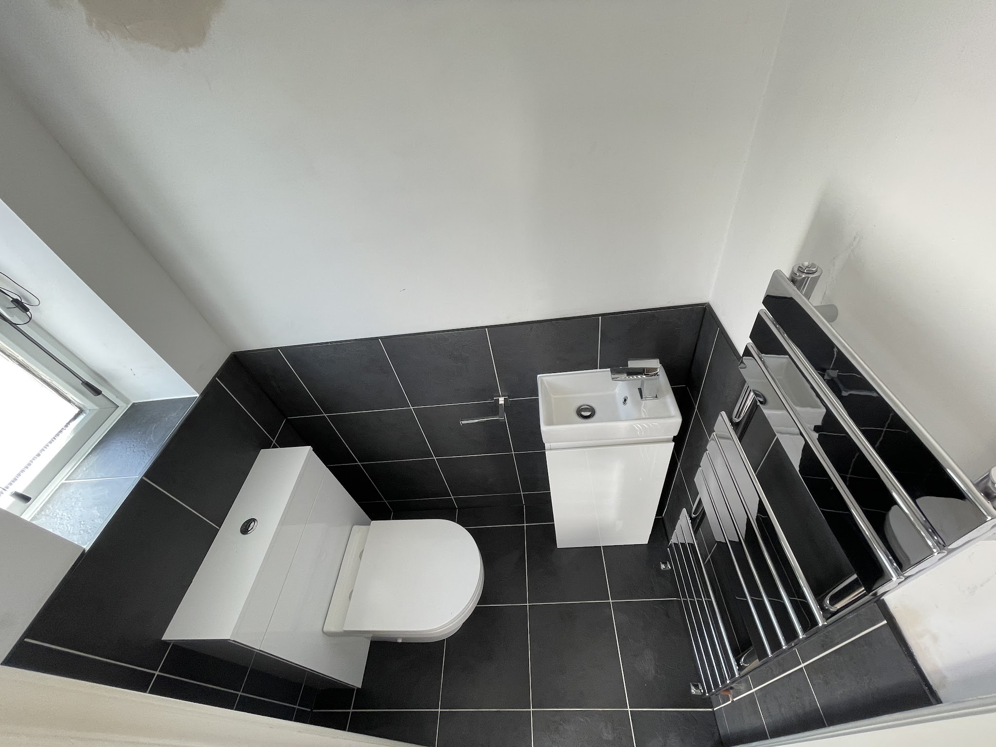 Compact cloakroom by Linden Whitehead seen from above: dark floor tiles, wall-hung toilet, small basin and chrome towel rail