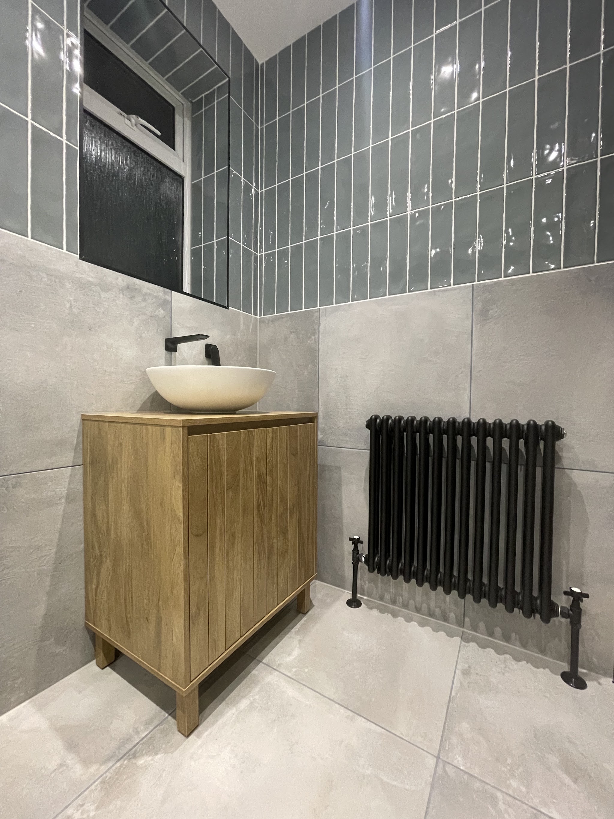 Oak vanity with a vessel basin and black tap beside a black column radiator, sage green metro tiles above