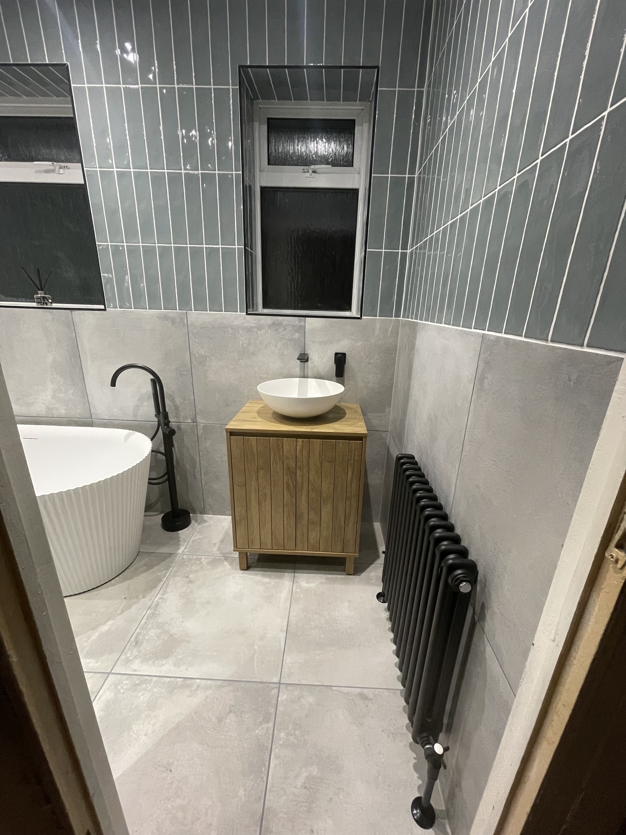 Bathroom with freestanding bath, oak vanity and column radiator against green metro tiling