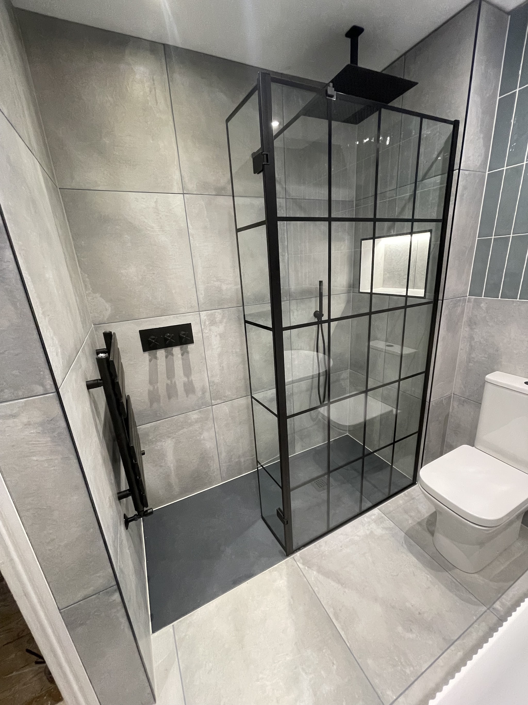 Black crittall-style walk-in shower enclosure with rainfall shower head and lit niche