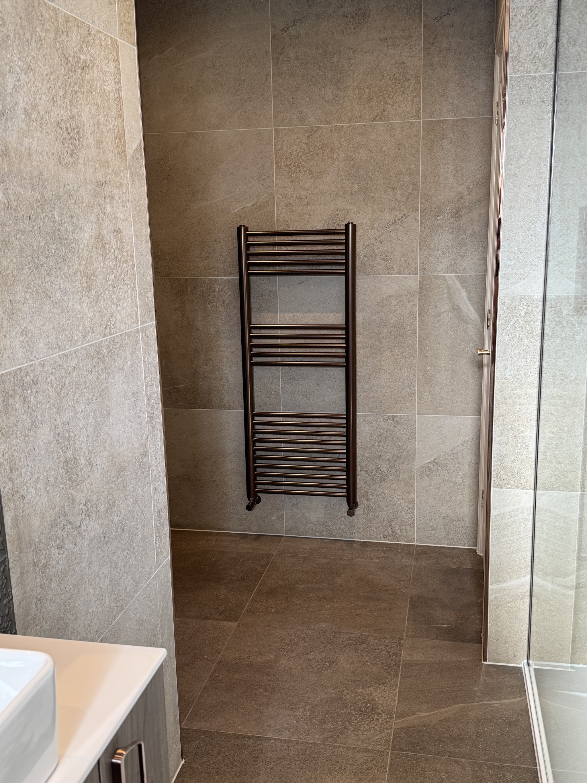 Black ladder towel rail fitted on warm stone-effect wall tiles